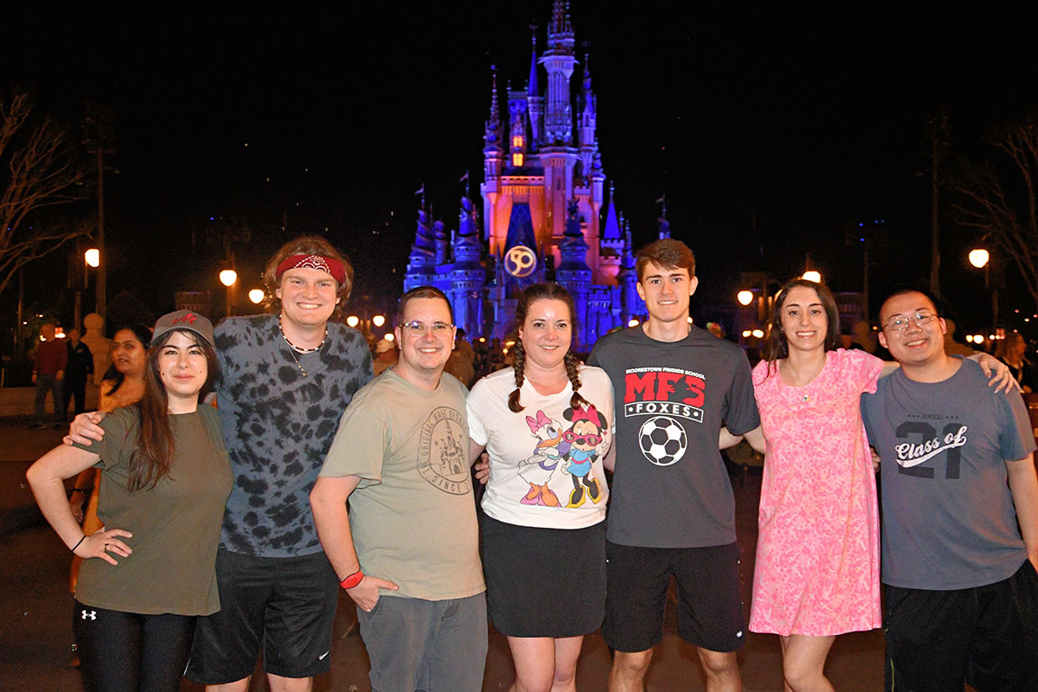 A group of 7 students smiling in front of Cinderella's Castle in Disney World at night